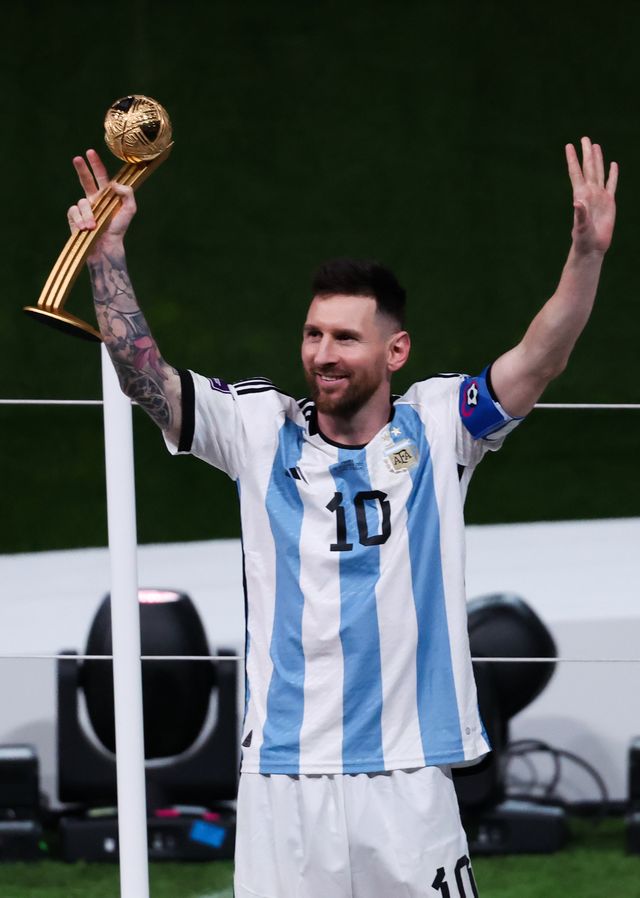 lionel messi holding a trophy with his right hand and waving his arms in celebration