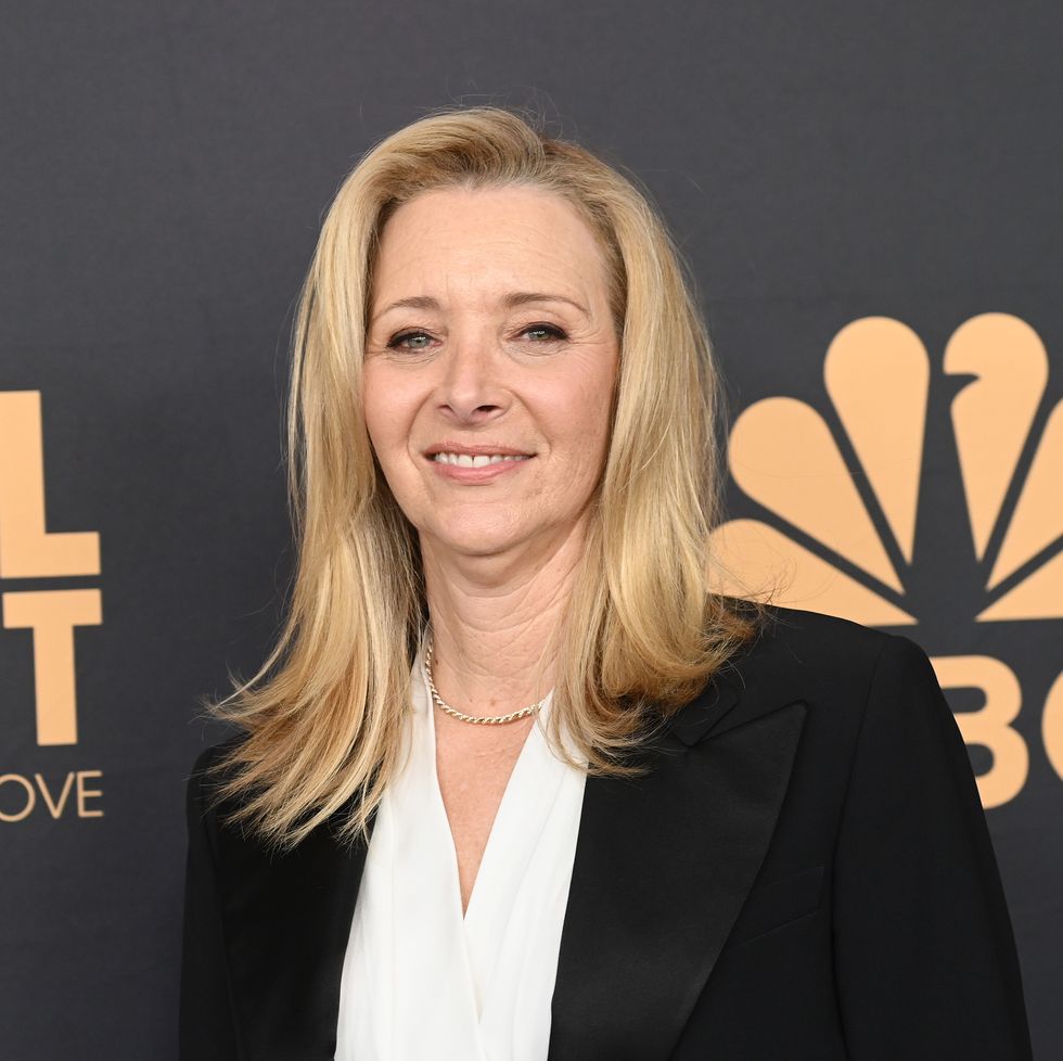 lisa kudrow smiles at the camera, she wears a black suit jacket and white blouse with a necklace
