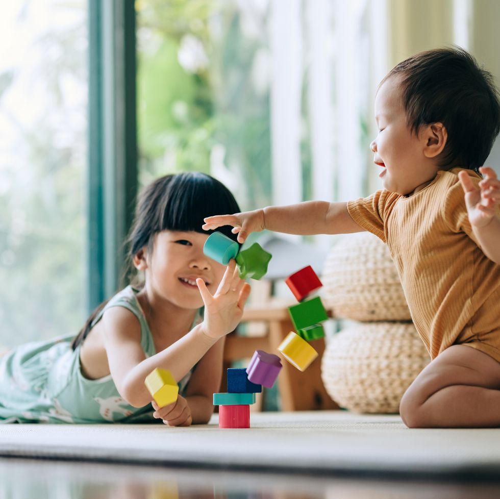 little asian girl and her baby sister playing colourful toy blocks together on the floor at home. two sisters having fun playing toys. siblings love. creative and curious children concept. sisters bonding moment. learning through play