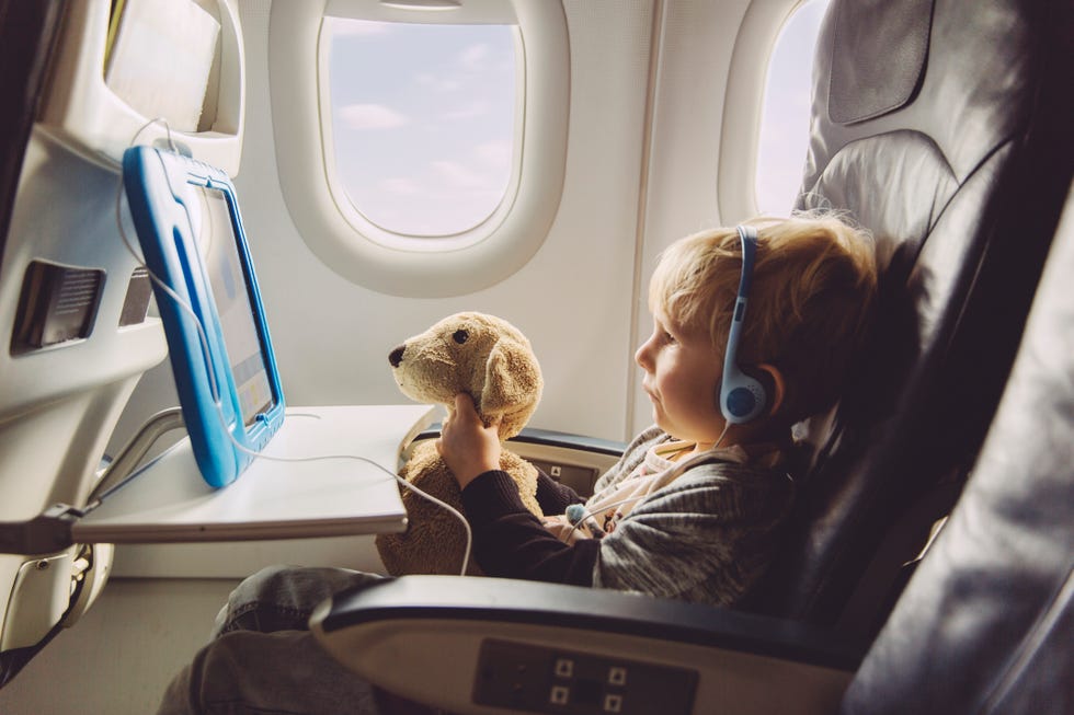 little boy sitting on an airplane watching something on digital tablet