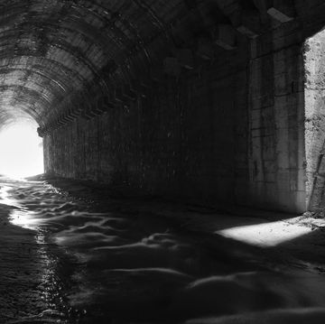 little creek flowing under old abandoned tunnel with safety starcaise