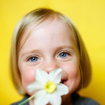 niña rubia de ojos claros oliendo flor