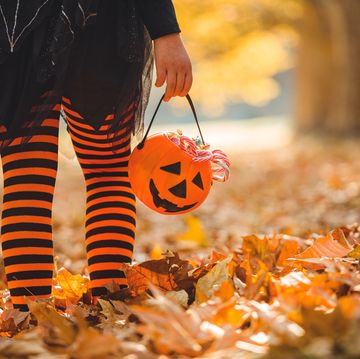 little girl in black and orange stockings walking in the leaves with a pumpkin purse full of candy