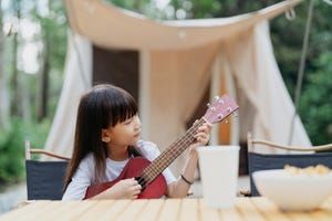 little girl playing ukulele while sitting on foldable chairs in the campsite