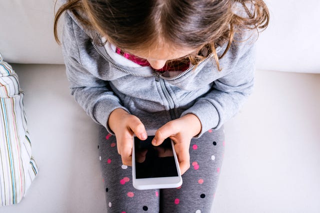 Little girl sitting on sofa, playing with smartphone