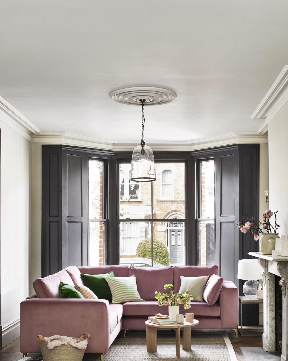 pink velvet corner sofa in living room with black panel window shutters