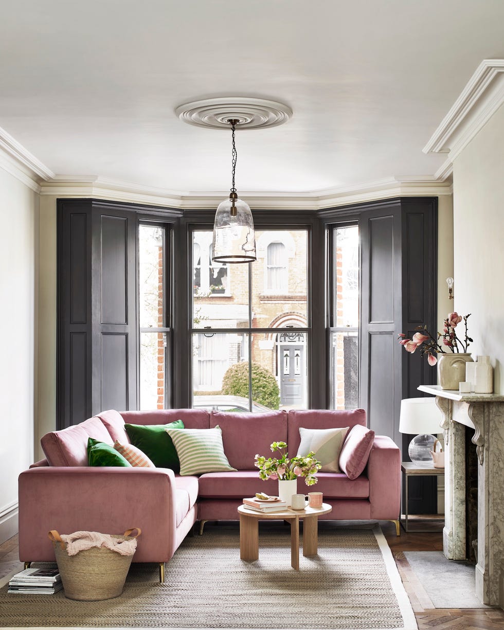 pink velvet corner sofa in living room with black panel window shutters