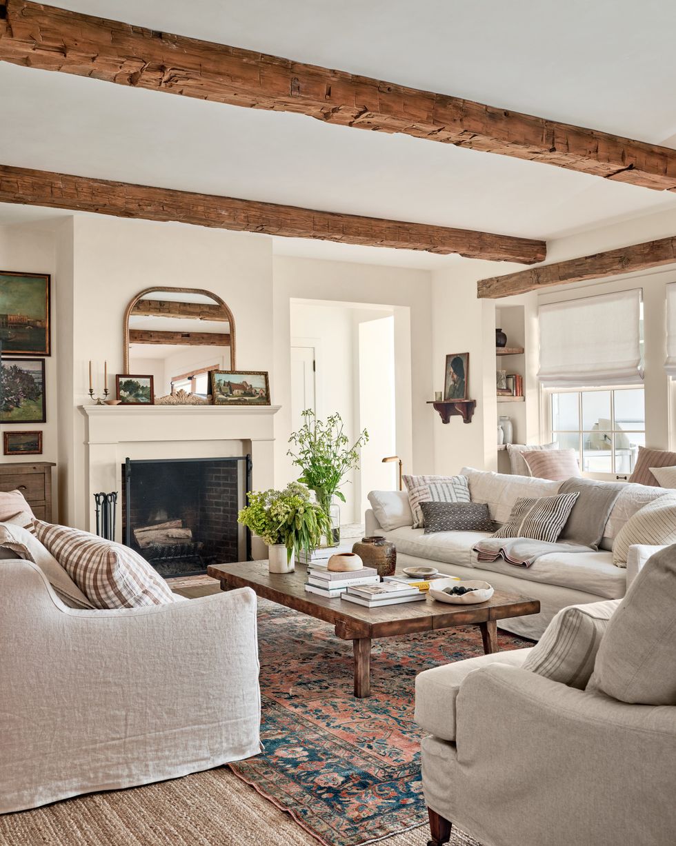 a living room with neutral furniture and walls and cool old ceiling beams