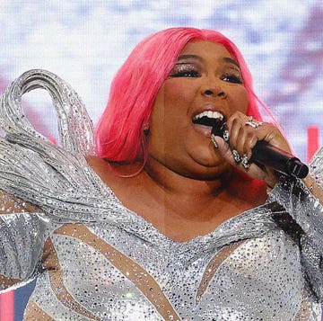 a photo of singer lizzo in a sequin jumpsuit with pink hair holding a mic on stage