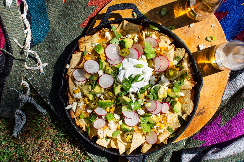 loaded campfire nachos in a cast iron skillet topped with corn, chunks of avocado, radish slices, sour cream, crumbled cheese, and cilantro