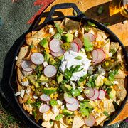 loaded campfire nachos in a cast iron skillet topped with corn, chunks of avocado, radish slices, sour cream, crumbled cheese, and cilantro