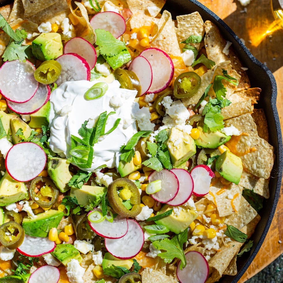 nachos in a skillet topped with corn, cilantro, and sour cream