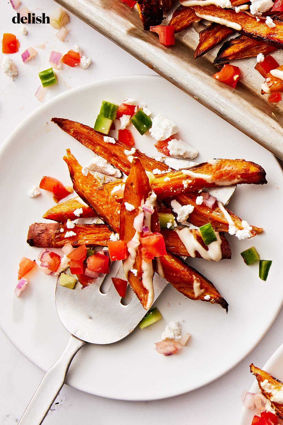 sweet potato fries topped with tomato and cucumber salad, tahini drizzle and feta