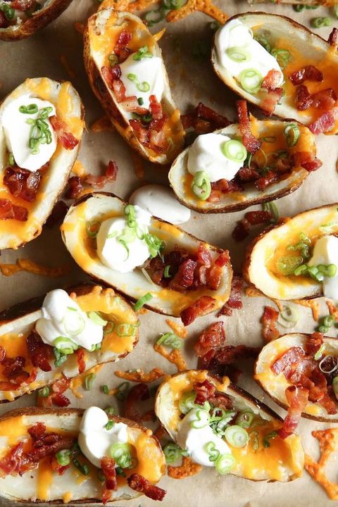 loaded baked potato skins topped with bacon, sour cream, melted cheese and scallions on a piece of parchment