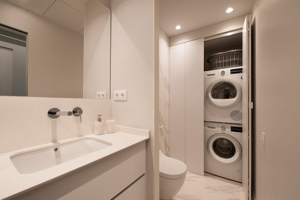 baño de color blanco con zona de lavandería escondida en los armarios