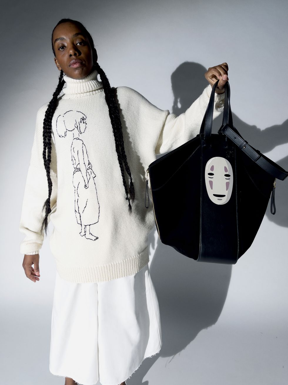 model wearing white sweater and pants holds up black tote bag