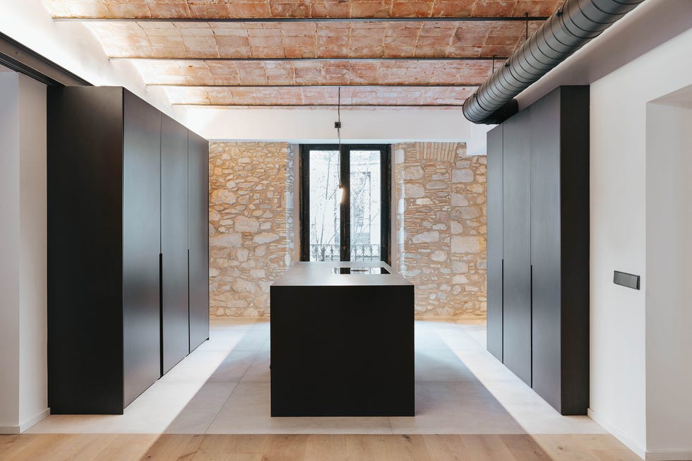 cocina de estilo industrial con isla central y paredes de piedra vista