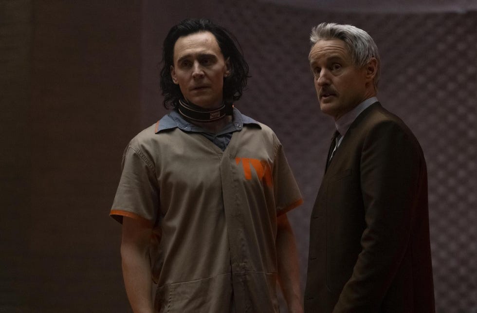 tom hiddleston as loki and owen wilson as mobius in loki, hiddleston wears a beige prison jumpsuit with tva logo