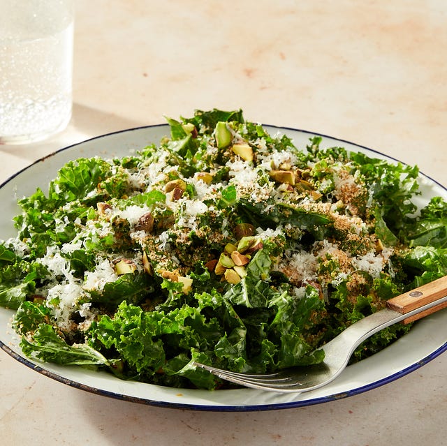 kale salad topped with cheese and pistachios in a white bowl with a blue rim on a marble background kale salad topped with cheese and pistachios in a white bowl with a blue rim on a marble background