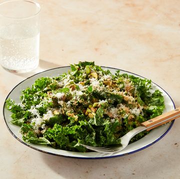 kale salad topped with cheese and pistachios in a white bowl with a blue rim on a marble background