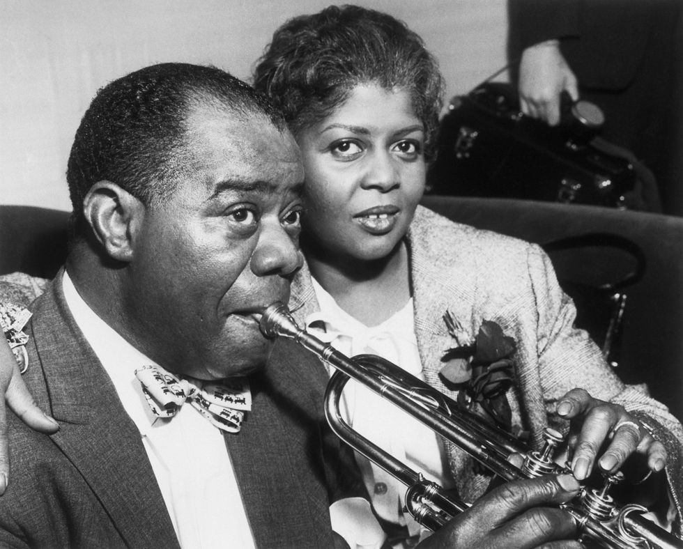 louis armstrong holding a trumpet to his mouth as his wife embraces him
