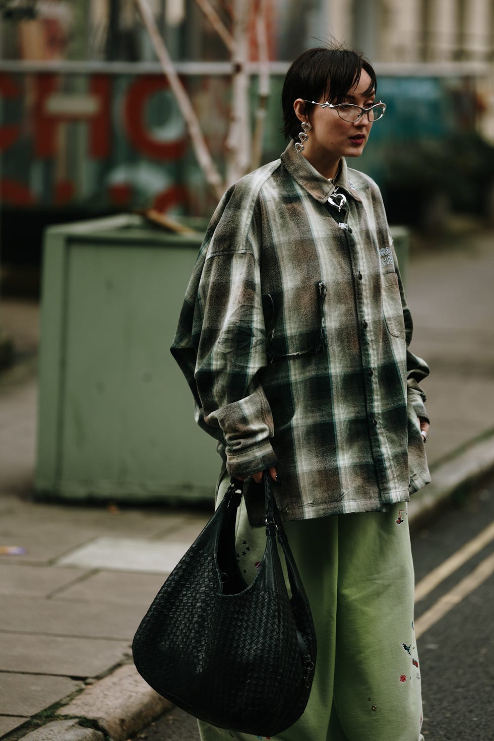 person wearing a plaid oversized shirt and green pants holding a black handbag best fringe haircuts london fashion week street style