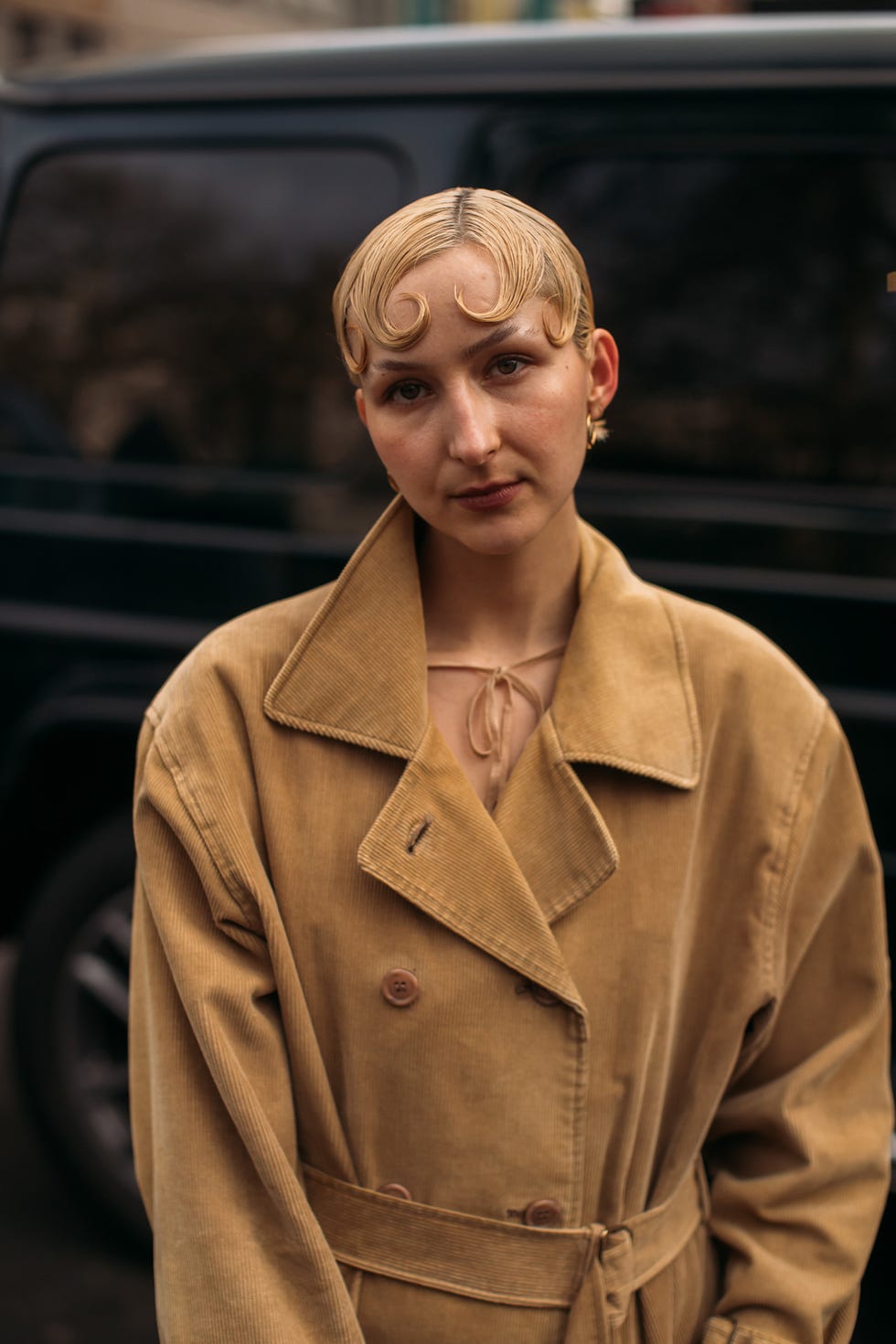 person wearing a beige trench coat in front of a dark vehicle best fringe haircuts london fashion week street style