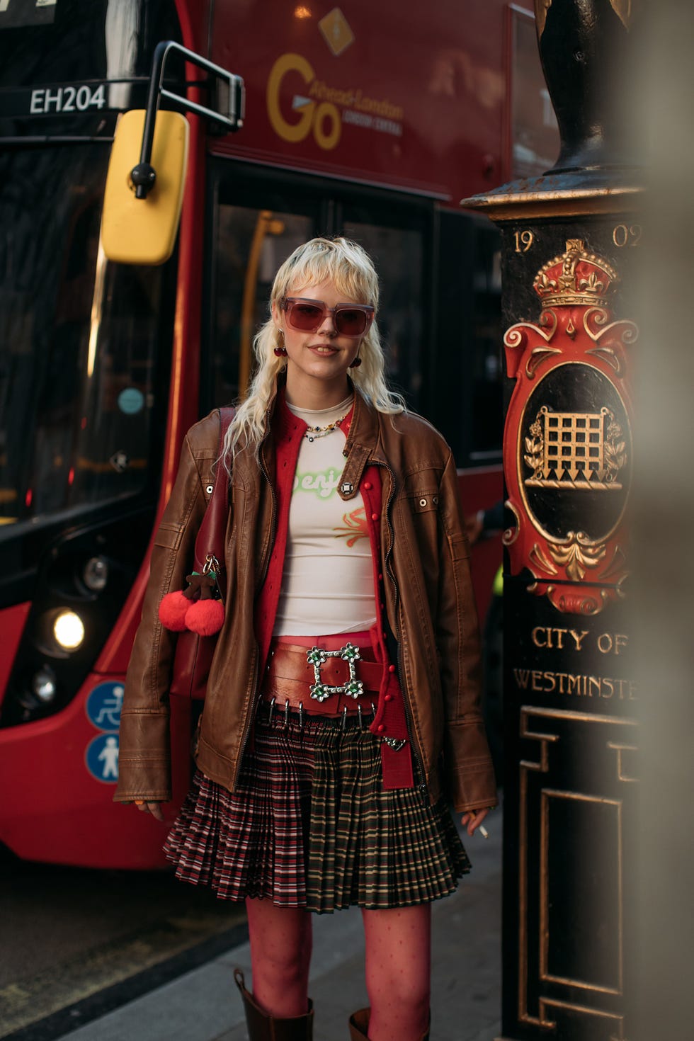 a person dressed in a distinctive urban outfit standing next to a red doubledecker bus best fringe haircuts london fashion week street style