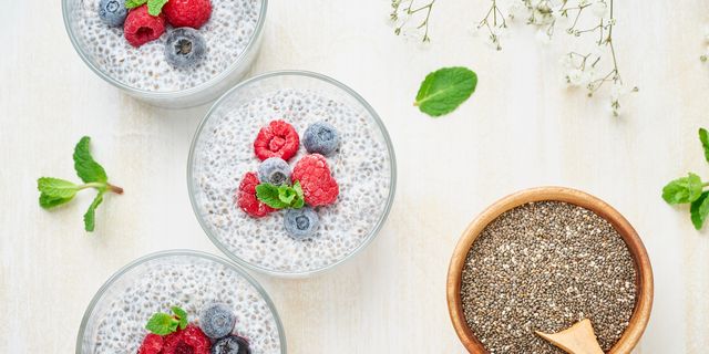 Long banner with chia pudding, top view, fresh berries raspberries, blueberries. Three glass, light wooden background, flowers.