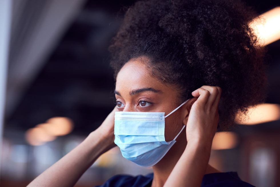 female doctor in scrubs putting on face mask under pressure in busy hospital during health pandemic