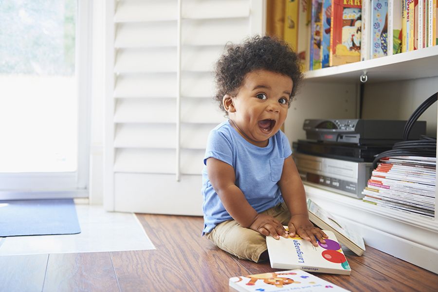 surprised black baby boy sitting on floor playing with books, used in a story about long names for boys