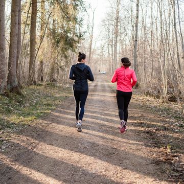 long shot of two sportive women running away from the camera in the forest.
