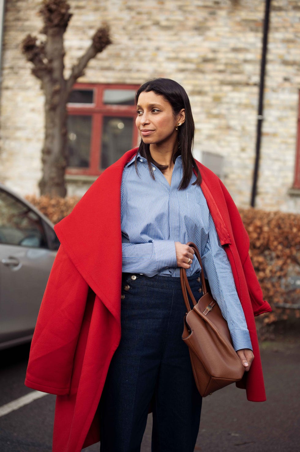 Fashionable individual wearing a red coat and striped shirt with brown bag