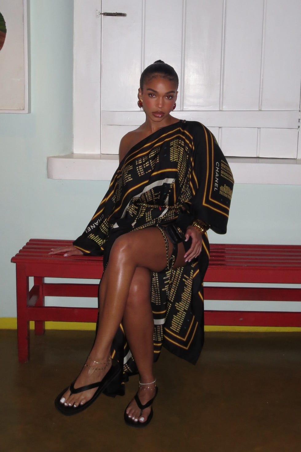 uma pessoa sentada em um banco vermelho vestindo uma roupa estampada em preto e dourado