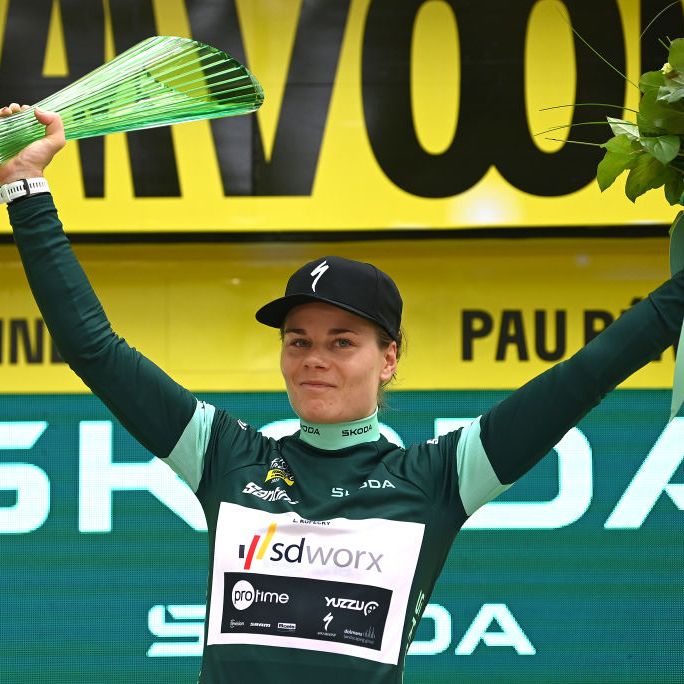 a cyclist wearing a green jersey holding a trophey on a podium