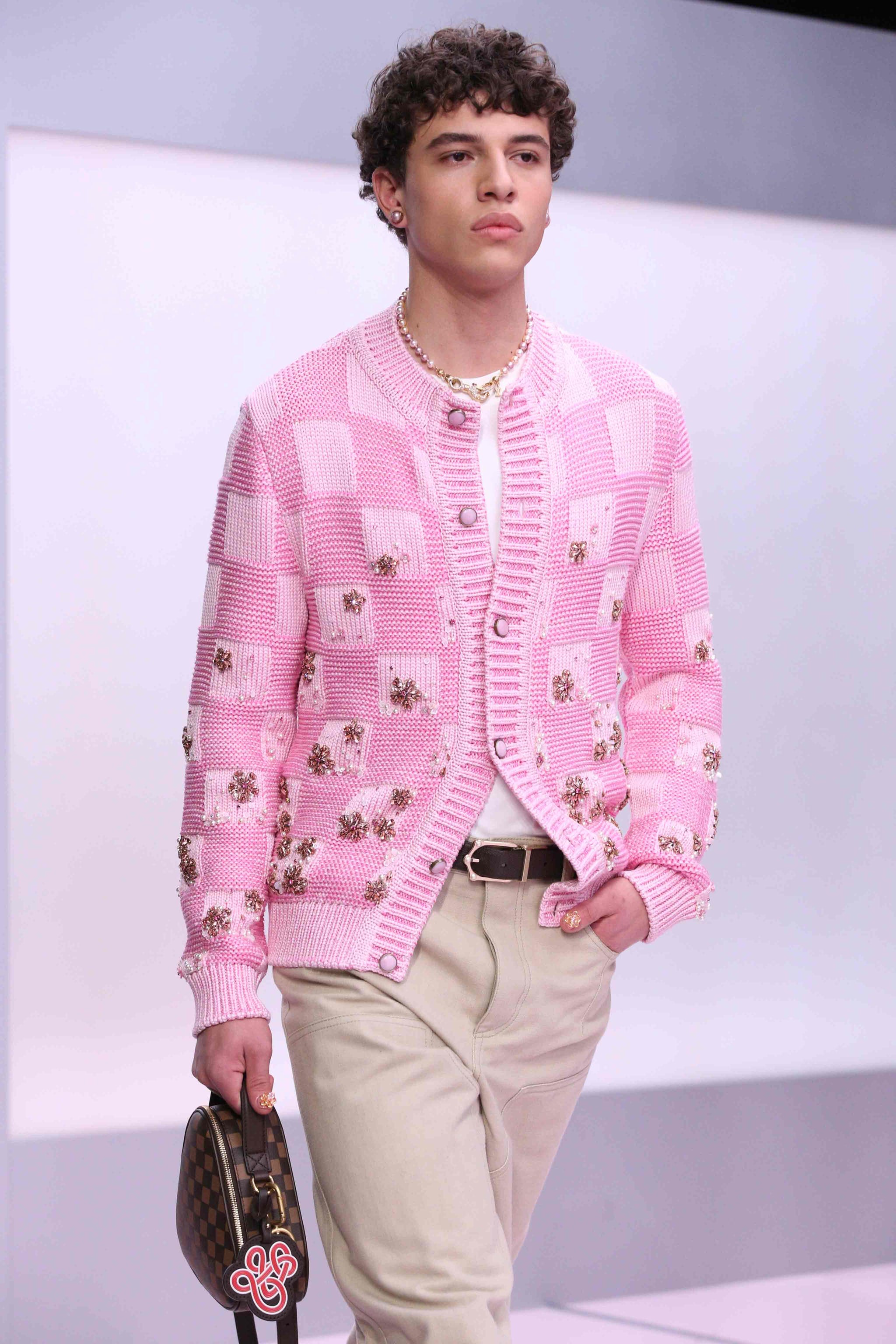 fashion model showcasing a stylish outfit featuring a pink knitted cardigan with floral embellishments and beige trousers