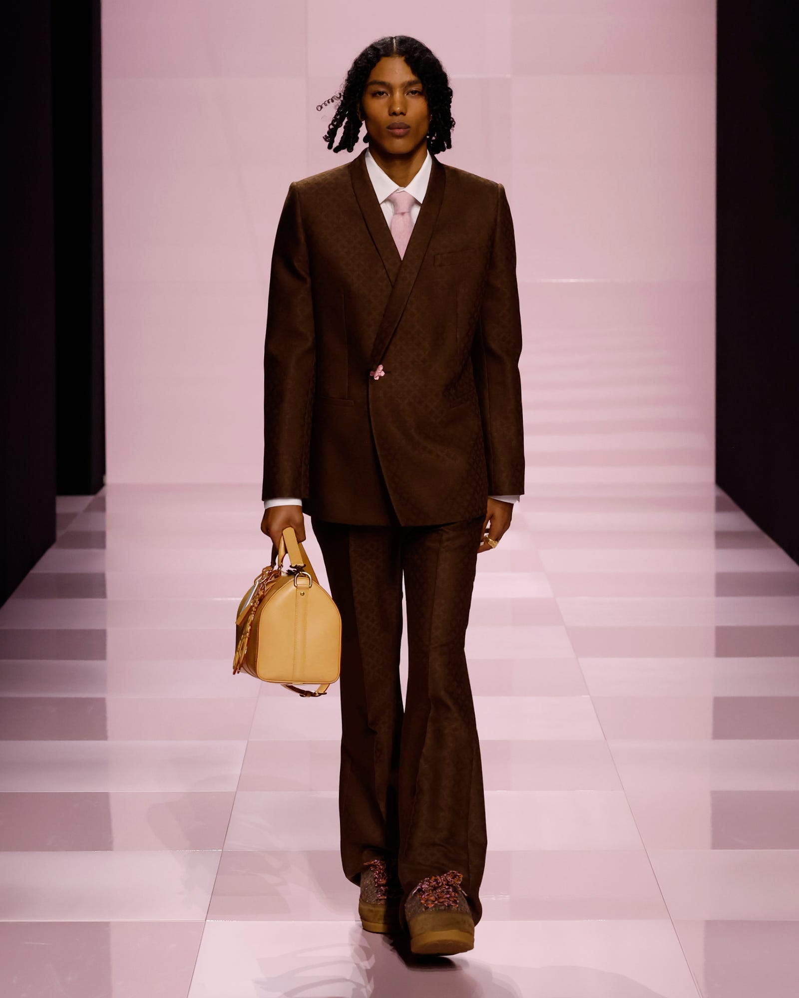 a model walking in a fashion show wearing a brown suit and holding a yellow handbag