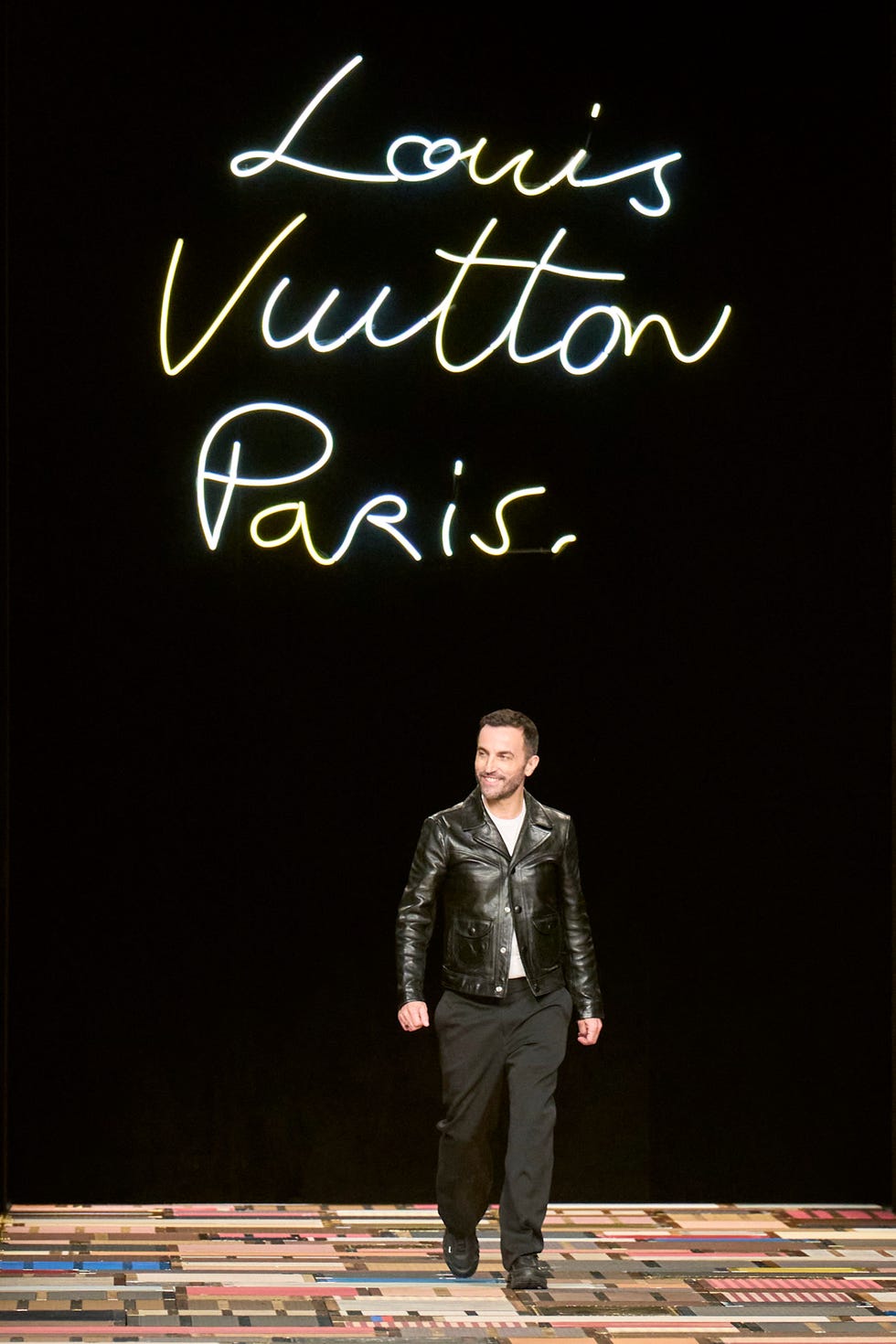 Male model walking down a runway with neon brand logo in the background