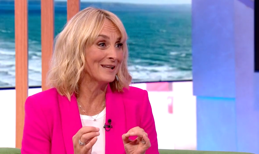 louise minchin, a woman sits on a sofa and talks to show hosts, she has lightly curled blonde hair and wears a white tshirt with bright pink suit