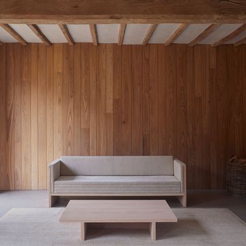 long wood daybed in simple elegant lines with velvet cushions and a simple matching cocktail table all against a panelled honey colored wall