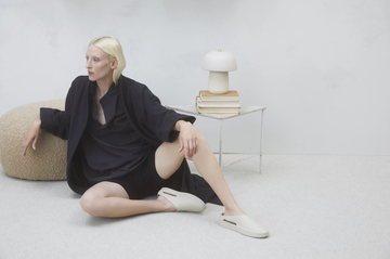 a model from fear of god wears a fear of god matching loungewear set while sitting in a white room in a roundup of the best loungewear sets to buy now 2021