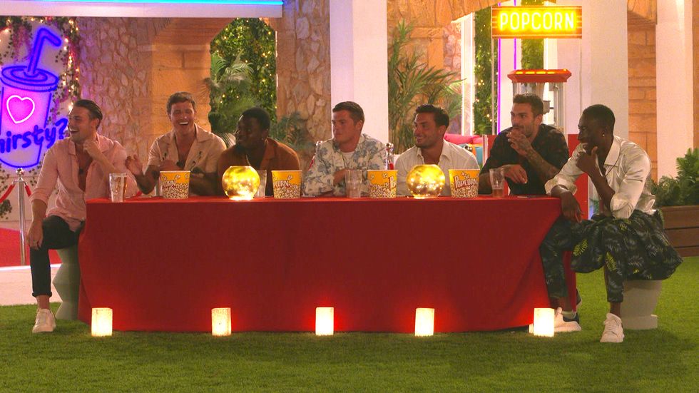andrew, luca, dami, billy, davide, adam and deji sit at a table watching a movie with popcorn on love island