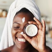 black woman right out of shower holding up moisturizer to face