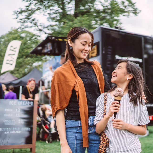 lovely girl enjoying ice cream with her young pretty mom in front of a food truck at food festival