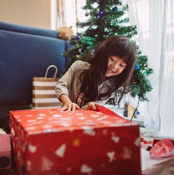 lovely little girl opening christmas presents at home joyfully