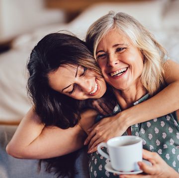 loving adult daughter embracing cheerful senior mother at home