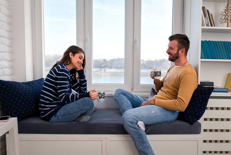 loving couple sitting together by the window in the apartment and drinking coffee in the morning