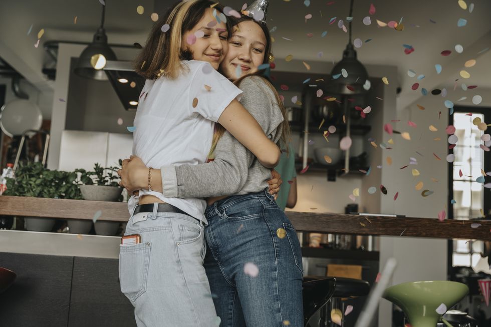 loving teenage friends embracing while standing in birthday party at home