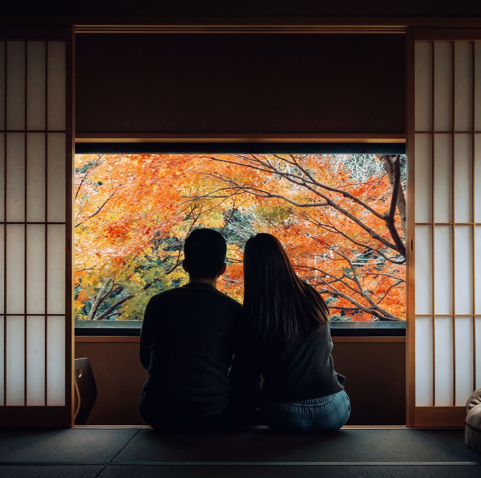 a loving young asian couple sitting side by side by the window in a traditional japanese style apartment, chatting and enjoying the beautiful nature autumn scenics during the day
