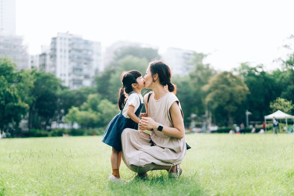 a loving young asian mother kissing and embracing her lovely little daughter in urban park, against beautiful sunlight precious moment between mother and daughter family lifestyle family love and care enjoying nature and summer days outdoor